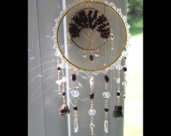 May include: A circular gold wire suncatcher featuring a central tree of life design crafted from dark red garnet gemstone chips. The outer ring is adorned with clear crystal beads, and multiple dangling strands feature garnet and clear crystal accents.