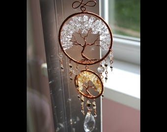 May include: A handcrafted copper wire tree of life suncatcher. The design features two circular frames, one filled with clear crystals and the other with yellow crystals. Additional clear and black beads dangle from the frames, with a large crystal at the bottom.