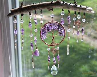 May include: A handcrafted dreamcatcher featuring a copper wire tree of life design filled with purple amethyst stones. Clear and purple beads, along with a large crystal pendant, hang from a wooden branch, creating a decorative and spiritual piece.