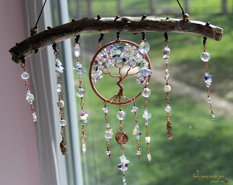 May include: A handcrafted dreamcatcher featuring a copper wire tree of life design, adorned with clear and purple gemstones, and hanging from a natural wooden branch. The dreamcatcher has multiple strands of beads and crystals.