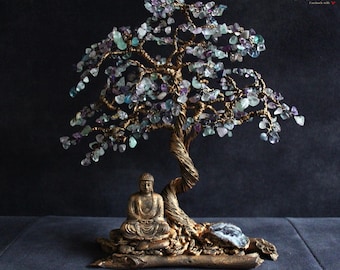 May include: A handcrafted wire tree sculpture with a bronze-colored trunk and branches, adorned with colorful gemstone leaves. A seated Buddha statue rests beneath the tree, creating a serene and decorative piece.