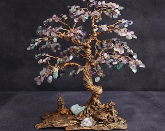 May include: A handcrafted wire tree sculpture with a bronze-colored base and trunk. The tree's branches are adorned with small, colorful gemstones in shades of purple, green, and clear. A miniature pagoda and crystals are at the base.