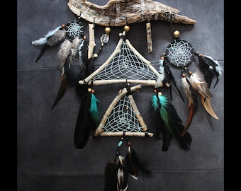 May include: A dreamcatcher with a triangular design, featuring black and white netting, turquoise beads, and feathers. The dreamcatcher is made of natural wood branches and is hung from a piece of driftwood.
