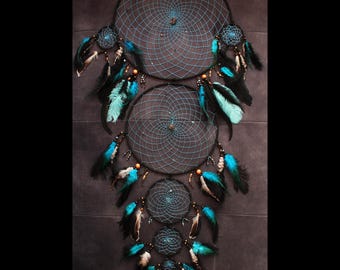 May include: A large dream catcher with four hoops, featuring black and turquoise colors. The dream catcher has feathers and beads hanging from the bottom.