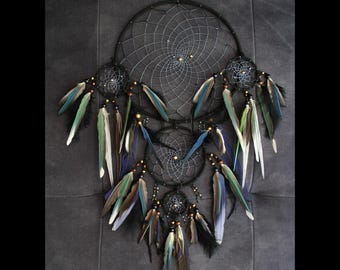 May include: A black dreamcatcher with multiple circular frames and a web-like design. It features colorful feathers in shades of blue, green, and white, and small decorative beads. The dreamcatcher is suspended against a dark background.