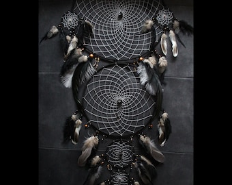 May include: A triple dreamcatcher with black and white netting, black beads, and brown feathers. The dreamcatcher is hanging against a dark gray background.