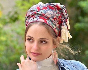 May include: A red and blue floral patterned headscarf with white fringe tassels. The scarf is tied in a knot on top of the head.