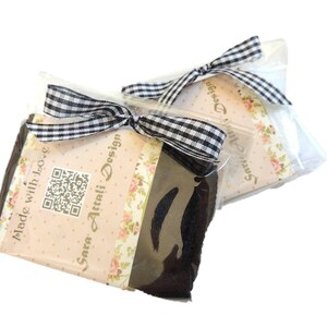 May include: A black and white checked ribbon tied around a package with a floral design and the text "Sara Attali Design" and "Made with Love".