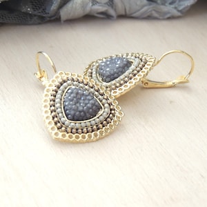May include: A pair of gold tone earrings with a gray triangle-shaped stone surrounded by gold beads and white beads.