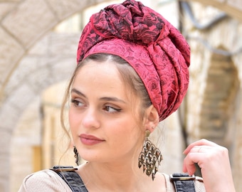 May include: A woman wearing a red and black floral patterned headscarf. The headscarf is tied in a knot at the top of her head. She is wearing large, dangling earrings.