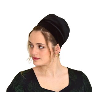 May include: A black velvet head covering with a satin trim. The head covering is worn by a person with dark hair.