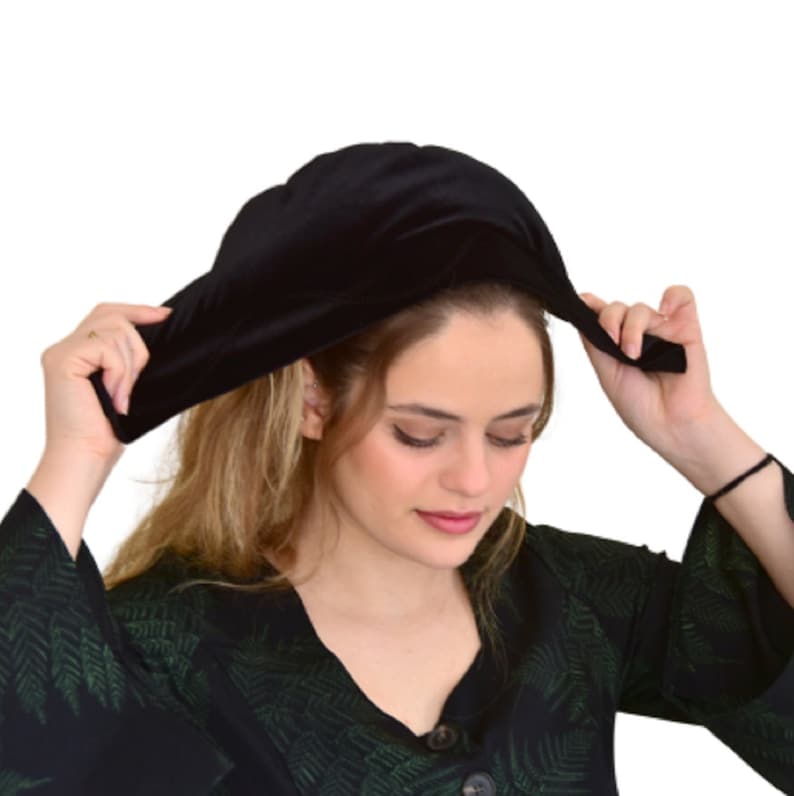 May include: A black velvet sleep cap with a wide brim. The cap is being held by a person's hands.