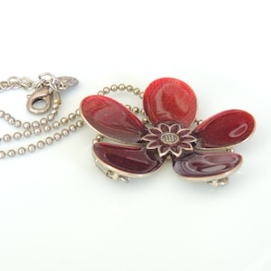 以下が含まれることがあります： 赤いエナメルの花のペンダントが付いたシルバーチェーンネックレス。花は5枚の花びらと小さなシルバーセンターを持っています。