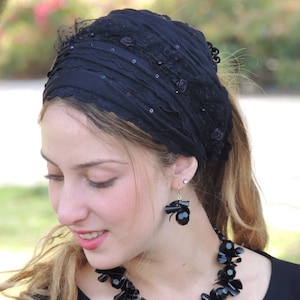 May include: A black headband with lace and sequins. The headband is worn by a person with long brown hair and black earrings.