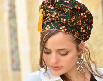 May include: A green headscarf with colorful embroidery and a gold tassel. The scarf is tied in a turban style and features a mirrored design.