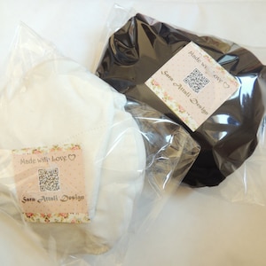 May include: Two white and black fabric squares packaged in clear plastic bags. Each bag has a label with a QR code and the text "Made with love" and "Sara Attali Design".