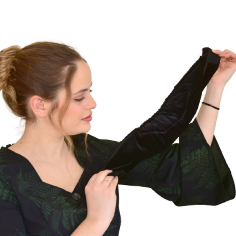 May include: A woman wearing a black and green dress with a black velvet sleeve. The sleeve is gathered at the elbow and has a ruffled appearance.