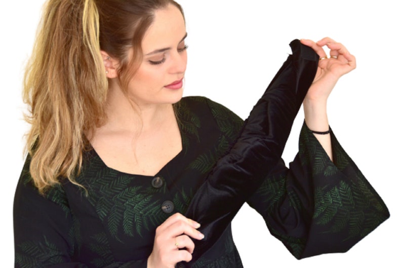 May include: A black velvet arm warmer with a green fern pattern. The arm warmer is being held by a person wearing a black dress with a green fern pattern.