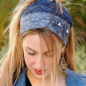 May include: A woman with long blonde hair is wearing a blue and grey headband with lace and pearl accents. She is wearing a denim jacket and has long, dangling earrings.
