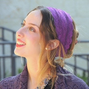 May include: A woman with long blonde hair wearing a purple lace headband. She is smiling and looking up.