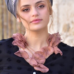 May include: A woman wearing a black shirt with a pink silk flower necklace. The necklace is made of multiple layers of silk flowers.