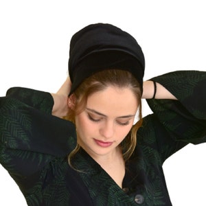 May include: A black velvet head covering with a wide brim. The head covering is worn by a person with long brown hair.