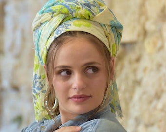 May include: A head covering with a floral pattern in shades of blue, green, and yellow. The fabric is wrapped around the head. The person is wearing a denim shirt and hoop earrings.