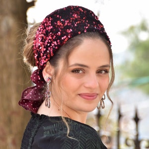 May include: A woman wearing a red and black sequined headband with a matching polka dot bow. The headband is tied in a knot at the back of her head.