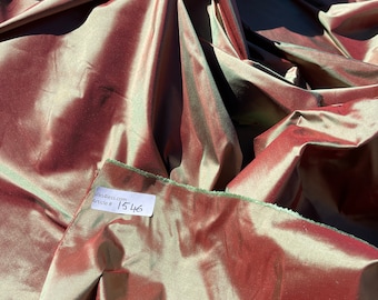 May include: A close-up of a piece of fabric with a green and red iridescent sheen. The fabric is folded and draped. A white tag with the text "silksdress.com Article # 1546" is attached to the fabric.
