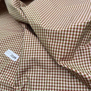 Op de afbeelding: Een close-up van een bruine en roze gingham stof. De stof heeft een klein ruitpatroon en is gevouwen op een manier die de textuur laat zien. Een liniaal is zichtbaar in de onderkant van de afbeelding, met de tekst "Article # 1009" zichtbaar op een wit label.