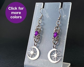 May include: A pair of silver earrings with a crescent moon and star design. The earrings have a purple chain with a silver bead.