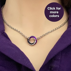 May include: A silver chain necklace with a ring pendant featuring three intertwined bands in black, purple, and white.