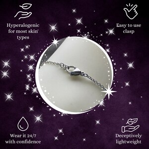 May include: A close-up of a silver chain necklace with a lobster clasp. The necklace is on a white surface and the background is a purple color with white stars.