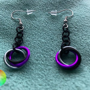 May include: A pair of dangle earrings with a black chain and a purple, black, and silver ring design.