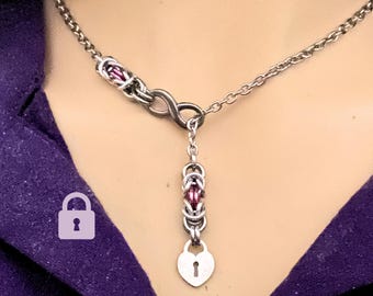 May include: A silver chain necklace with a heart-shaped pendant and a small lock. The chain is made of interwoven metal rings with purple beads.