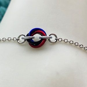 May include: A silver chain bracelet with a red, blue, and black woven ring charm.