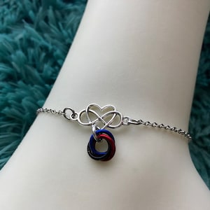 May include: A silver chain bracelet with a heart-shaped charm and a charm with three intertwined rings in red, blue, and black.