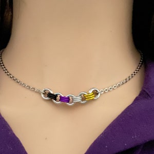 May include: A silver chain necklace with four linked rings. The rings are wrapped in purple, black, white, and yellow thread.