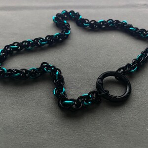 以下が含まれることがあります： 黒とターコイズブルーのチェーンネックレスで、黒い金属製のリング留め具が付いています。
