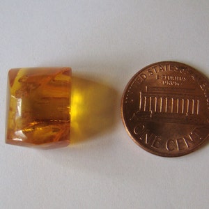 May include: A clear, amber-coloured, faceted glass bead, approximately the size of a UK penny.