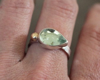 May include: A silver ring featuring a teardrop-shaped green gemstone and a gold accent.