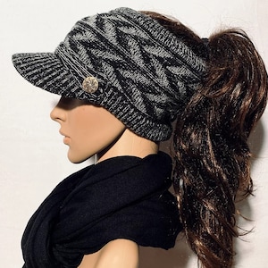 May include: A black and gray knitted beanie with a ponytail hole and a brim. The beanie has a button on the side.