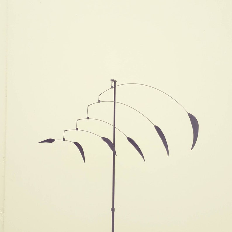 May include: A black metal mobile sculpture with multiple curved arms and hanging pieces. The sculpture is suspended from a single vertical pole.