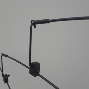 May include: Black metal clothing rack with multiple arms and a hook at the top. The rack is designed to hang clothes.