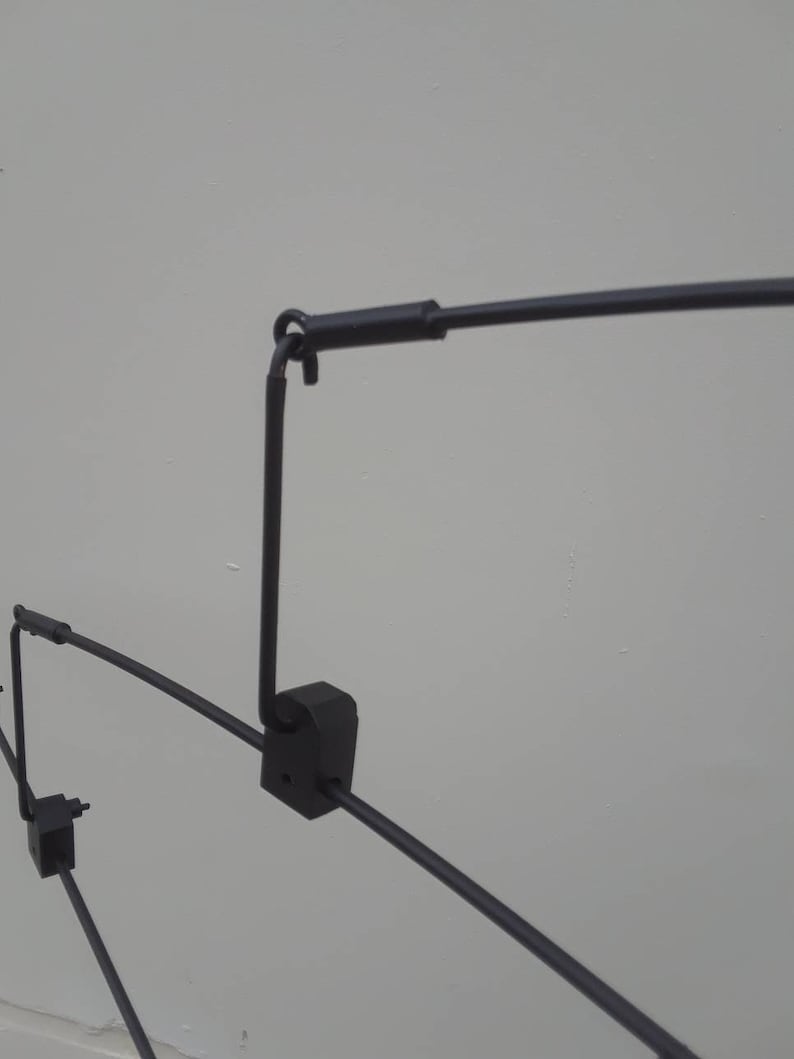 May include: Black metal clothing rack with multiple arms and a hook at the top. The rack is designed to hang clothes.