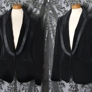 Può includere: Un blazer di velluto nero con revers in raso e chiusura a un bottone. La giacca è esposta su un manichino, mostrando la sua vestibilità su misura e il design classico. Il blazer ha due tasche anteriori.