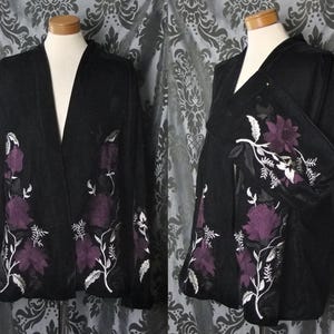 May include: Black open-front jacket featuring embroidered purple and white floral patterns. The jacket is displayed on a mannequin, highlighting the detailed embroidery and the drape of the fabric. The jacket's length is approximately 76 cm.