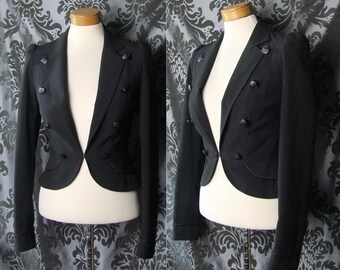 May include: A black cropped blazer with a double-breasted closure and gold buttons. The blazer has a fitted silhouette and a pointed collar.