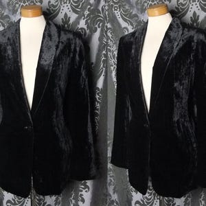 May include: A black velvet blazer on a mannequin. The blazer features a classic notched lapel, a single-button closure, and long sleeves. The fabric has a textured appearance. The image shows the blazer from two different angles.