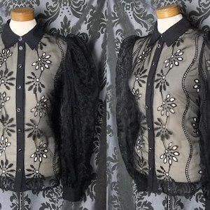 May include: Black button-down blouse with sheer sleeves and a floral design. The blouse features a black collar and cuffs, with a central panel adorned with embroidered white flowers. The sleeves are made of a delicate, lacy fabric.